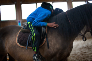 person riding horse in an equine therapy program gives the horse a hug