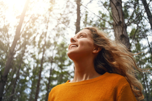 woman in orange sweater looks up in the woods while thinking about a mood disorder treatment program